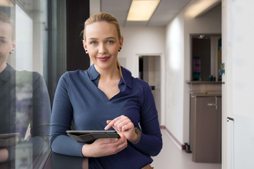 Eine Qualitätsmanagementbeauftragte steht in einem Klinikflur und arbeitet mit einem Tablet.